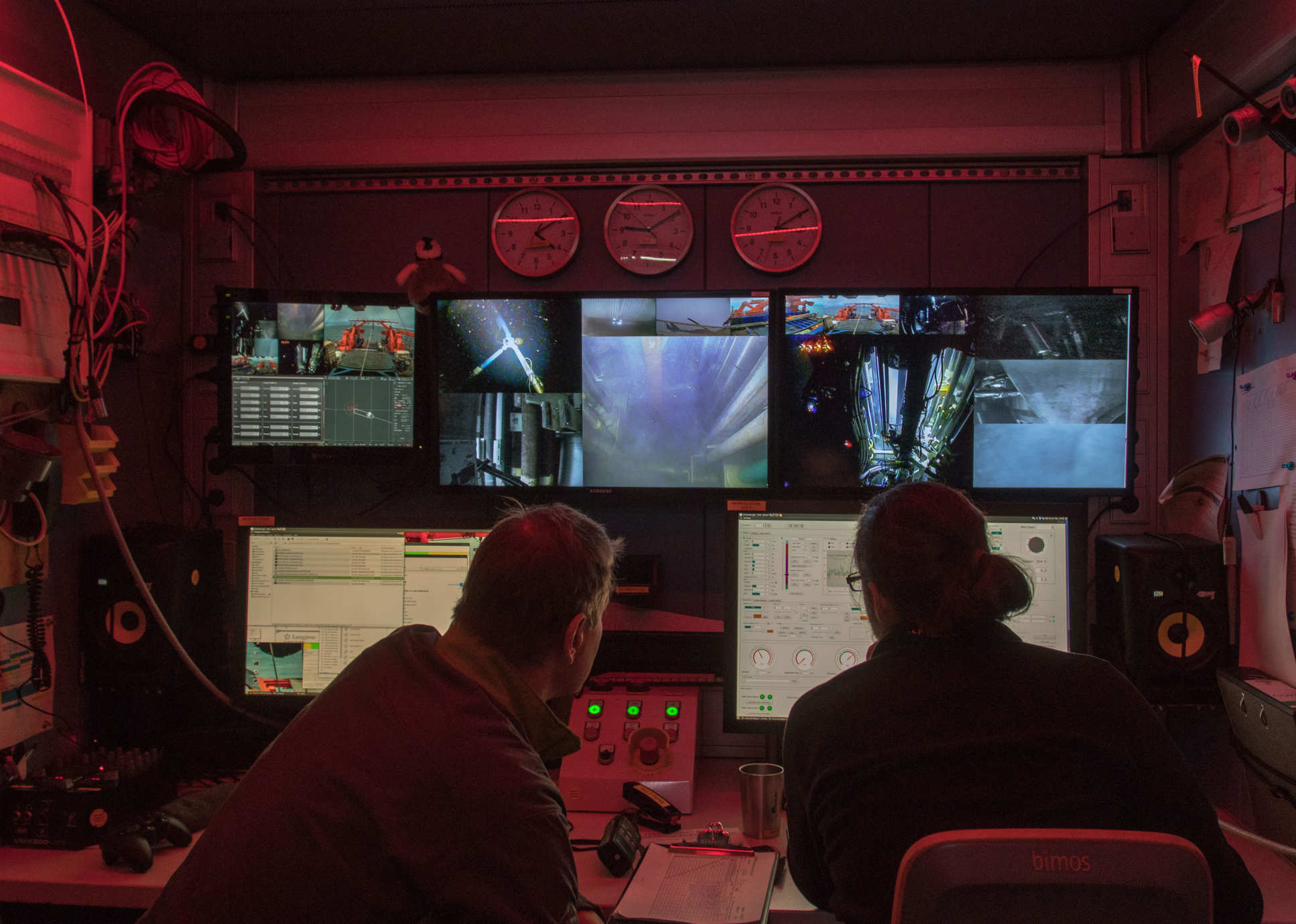 Two people in a dark room in front of screens showing ocean drilling