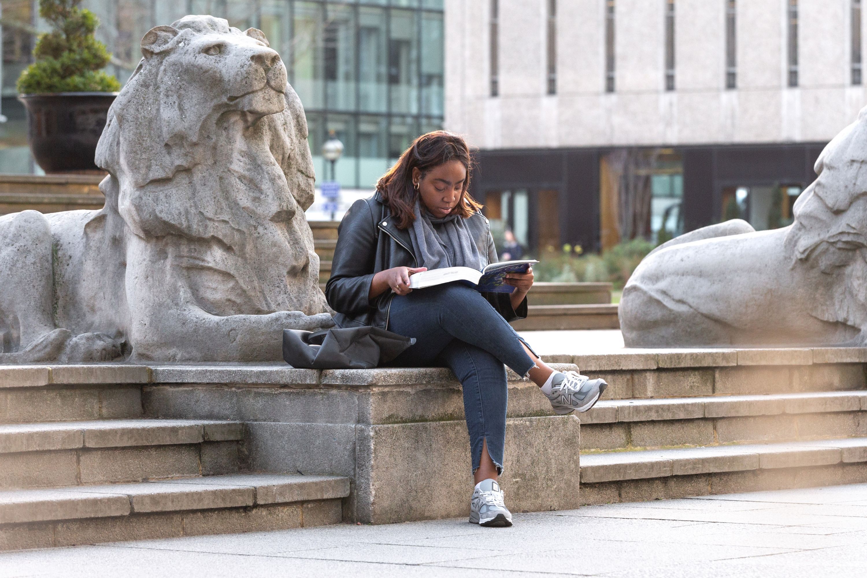 A student sat next to the Imperial lions reading