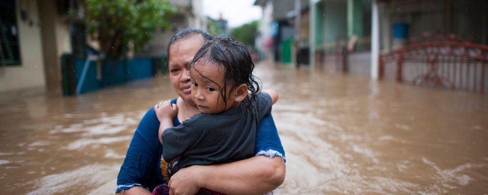 woman carrying child through flooded streets