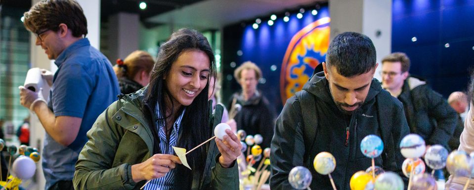 A man and a woman attending Imperial Lates, smiling while building miniature planets on sticks