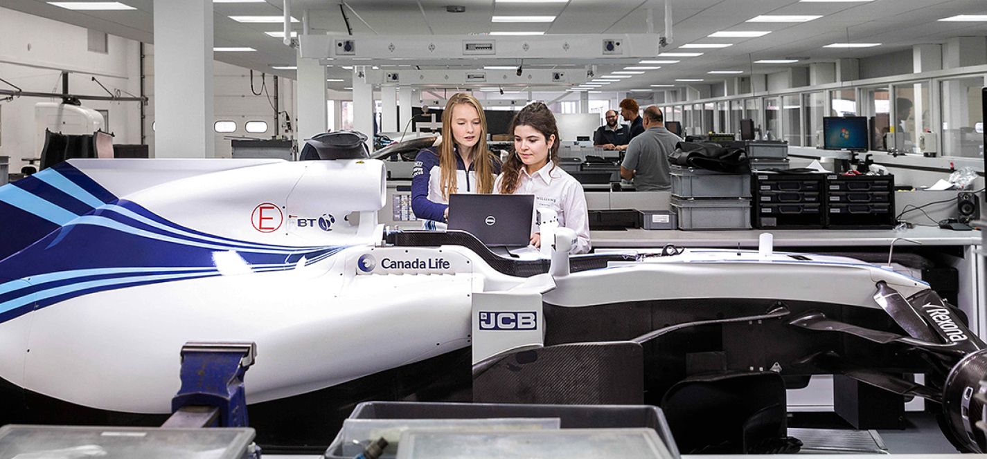 Two femaie Aeronautical Engineering students working next to a formula one car at WIlliams Racing in Oxford